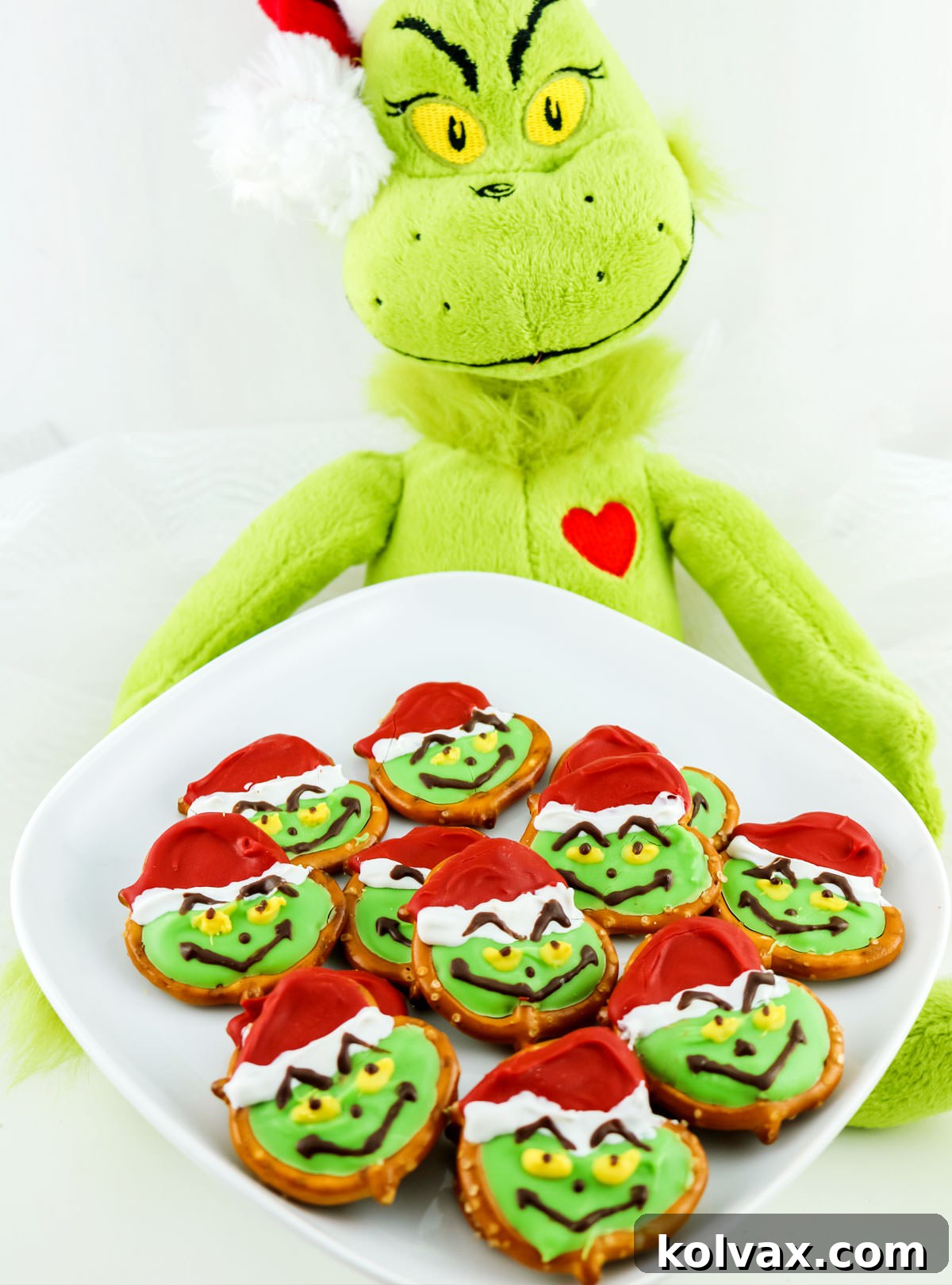 Closeup on a Grinch doll holding a white serving platter filled with Grinch Pretzels, ready for a Christmas celebration.