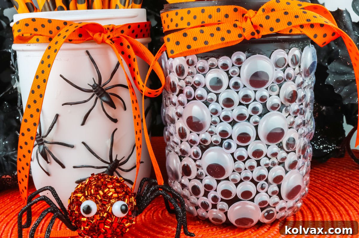 Two Spooky Halloween Mason Jars on an orange placemat, one covered in googly eyes and the other with plastic spiders, surrounded by festive Halloween decorations.