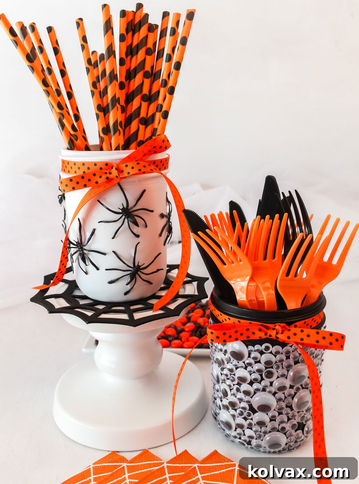 Two completed Spooky Halloween Mason Jars, one with googly eyes and the other with spiders, creatively displayed on a white table amidst Halloween candies and festive decorations, ready for a party.