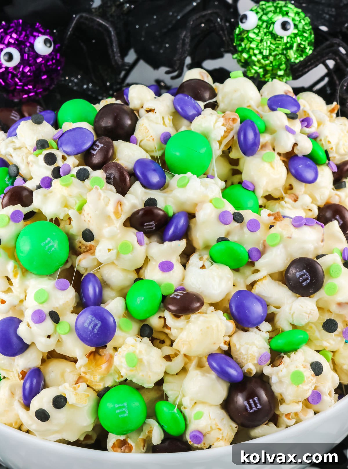 Closeup on Bewitched Halloween Popcorn in a white serving bowl sitting in front of Halloween Decorations, ready to be served.