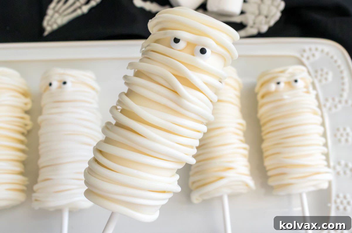 Closeup on a white dessert platter filled with a batch of Mummy Marshmallow Pops, showcasing their spooky and sweet details.