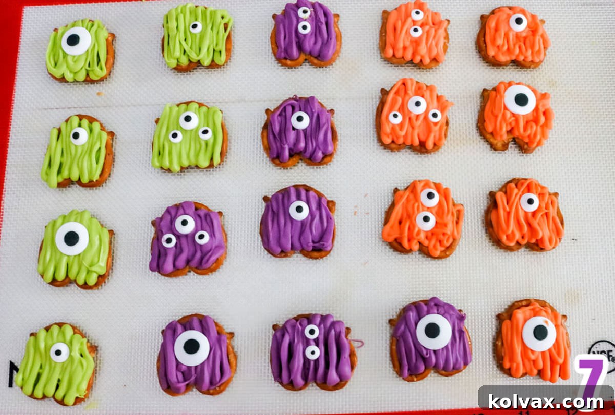 A baking sheet filled with an array of freshly made Monster Pretzel Bites in green, orange, and purple, adorned with varying numbers of googly eyes, waiting to dry.