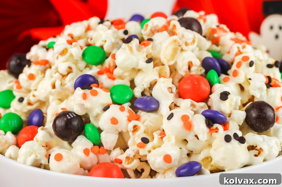 Closeup on a white serving bowl filled with Trick of Treat Halloween Popcorn with ghosts in the background.