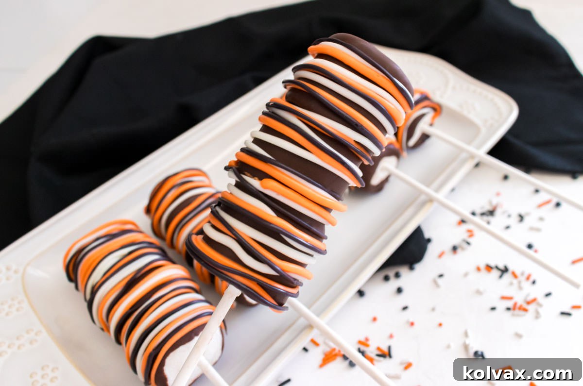 Wicked Marshmallow Wands 2 Closeup on a Halloween Marshmallow Pop hovering over a white dessert plate filled with more marshmallow pops, showcasing their vibrant decorations.