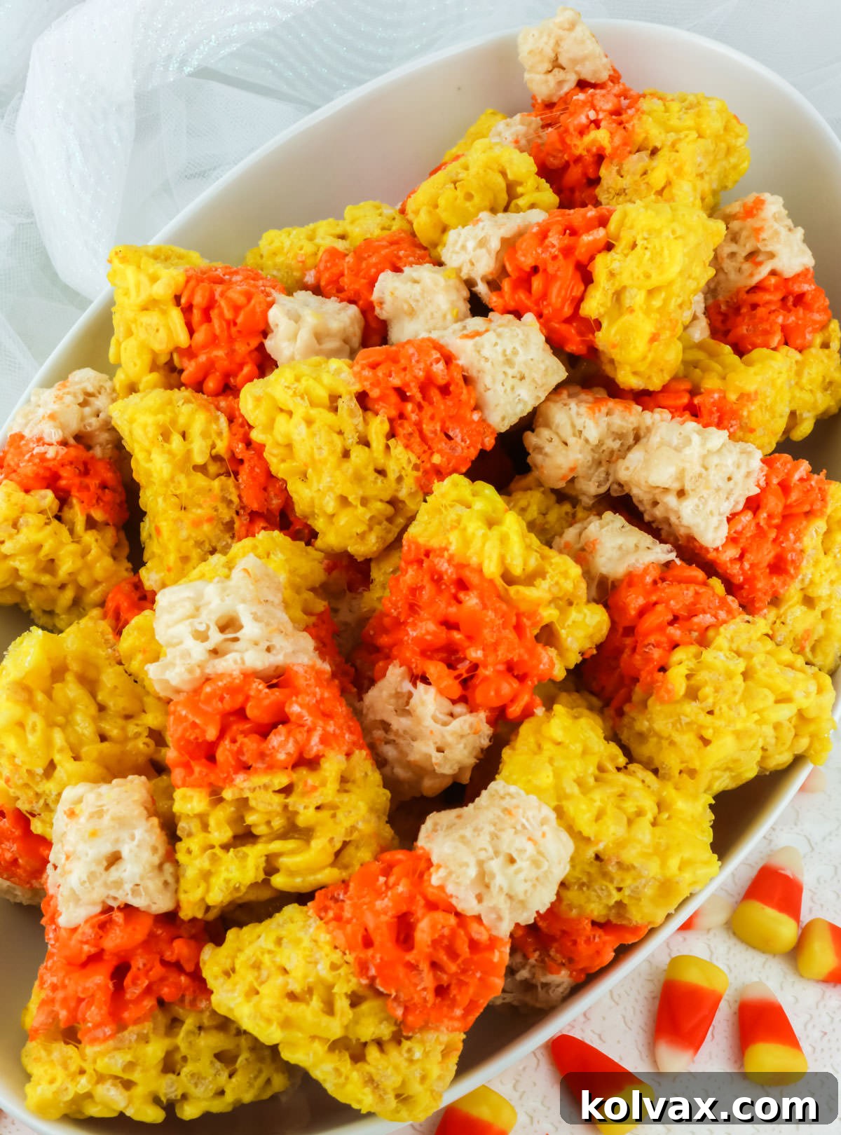Candy Corn Crunch Bars 8 Closeup on a white serving bowl filled with Candy Corn Rice Krispie Treats surrounded by real Candy Corn candies.