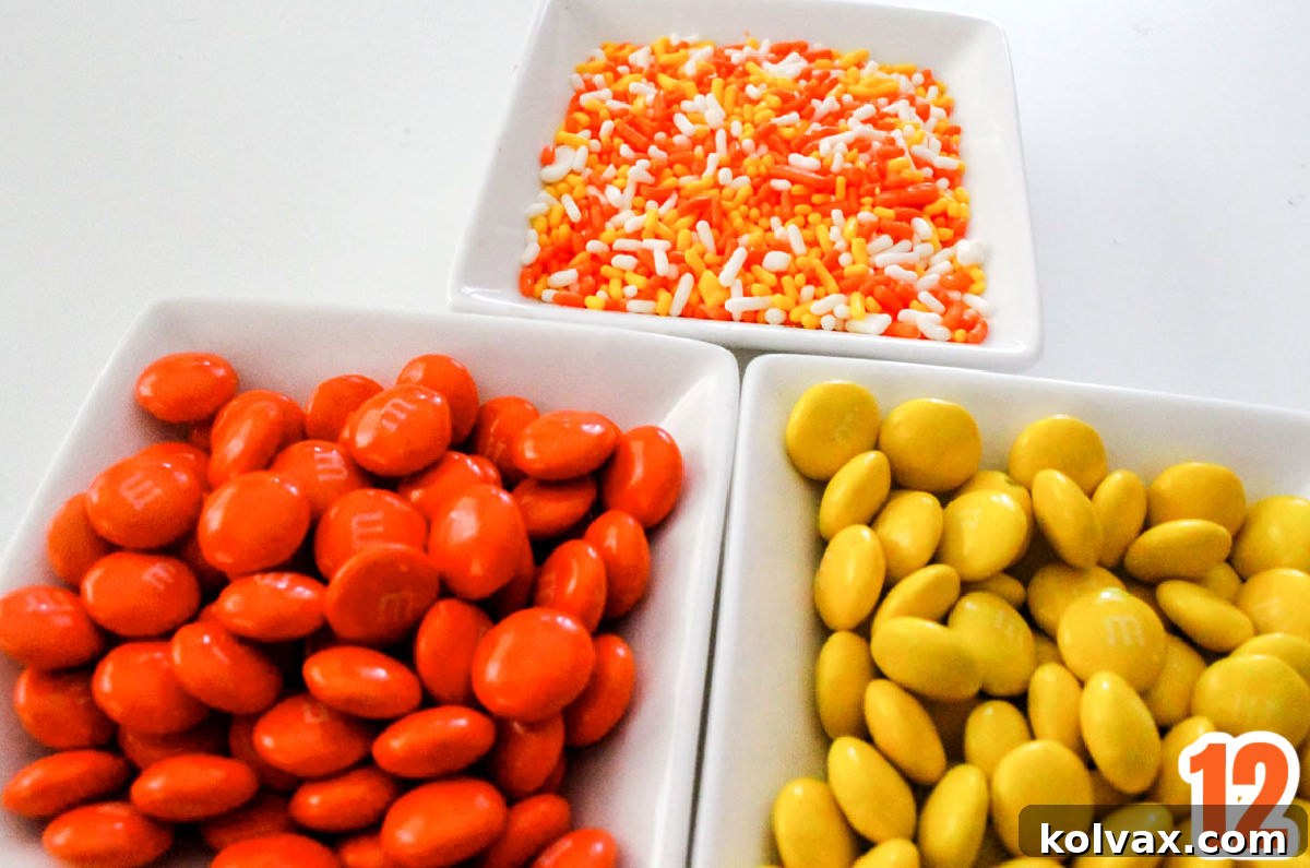 Three white ramekins filled with orange M&M's, Yellow M&M's, and Halloween sprinkles.
