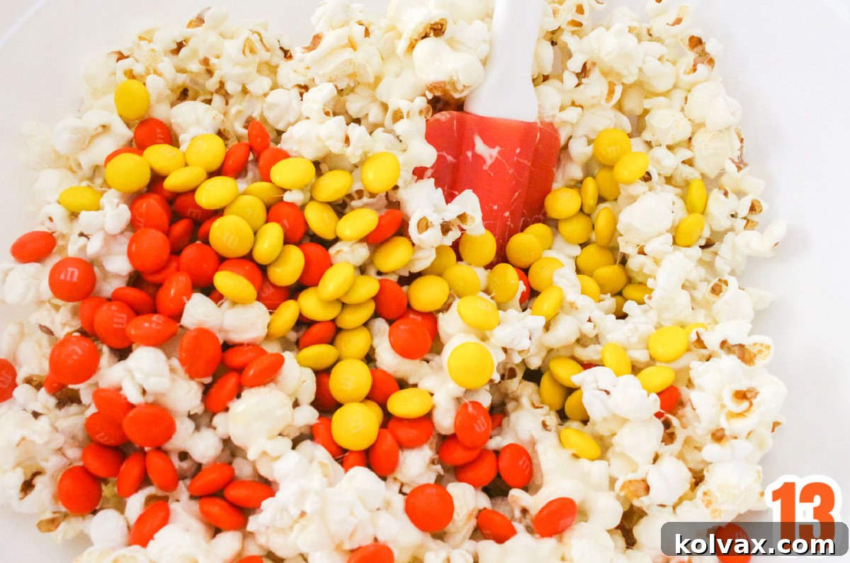 Closeup on a white mixing bowl filled with marshmallow popcorn and M&M's, ready for forming into balls.
