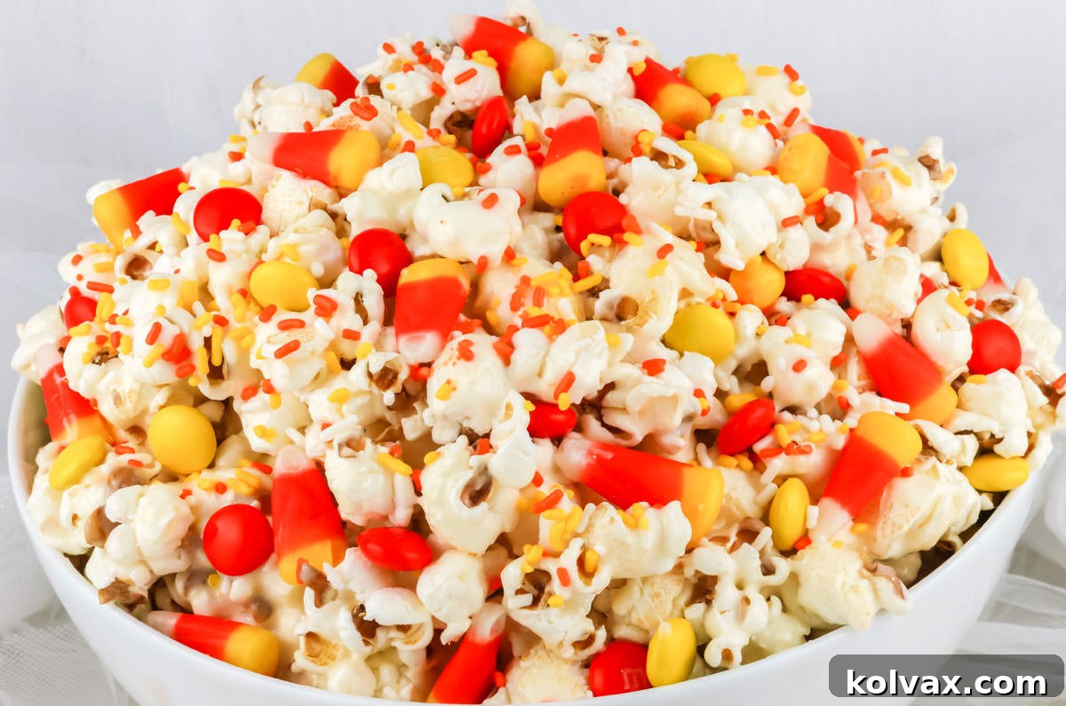 Closeup on a batch of Fall Candy Corn Popcorn in a white serving bowl sitting on a white surface, showcasing the vibrant colors and appealing texture.