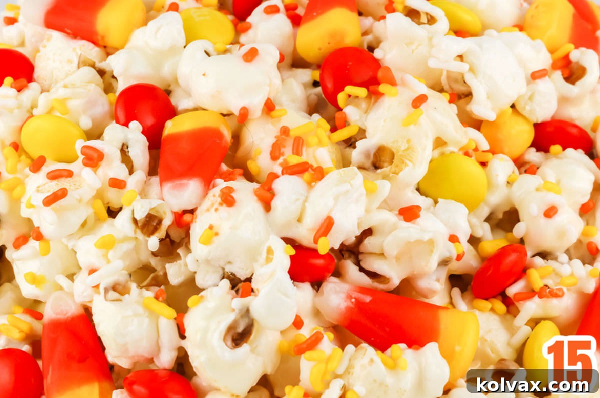 Closeup on a batch of Fall Candy Corn Popcorn, highlighting the perfectly coated marshmallow popcorn, scattered candy corn pieces, vibrant yellow and orange M&M's, and delicate sprinkles.