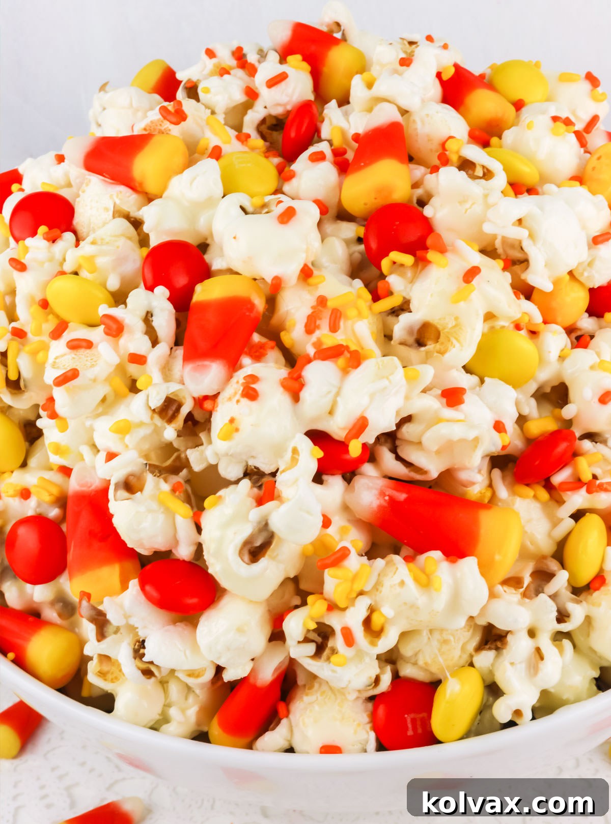 Closeup on a white serving bowl generously filled with vibrant Fall Candy Corn Popcorn, ready to be enjoyed.