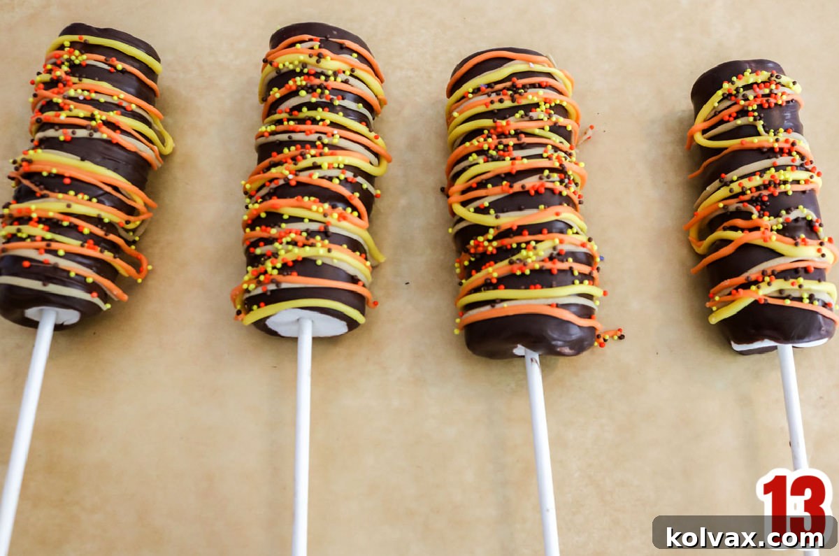 Four Harvest Marshmallow Pops laying neatly on parchment paper, adorned with colorful candy melt drizzles.