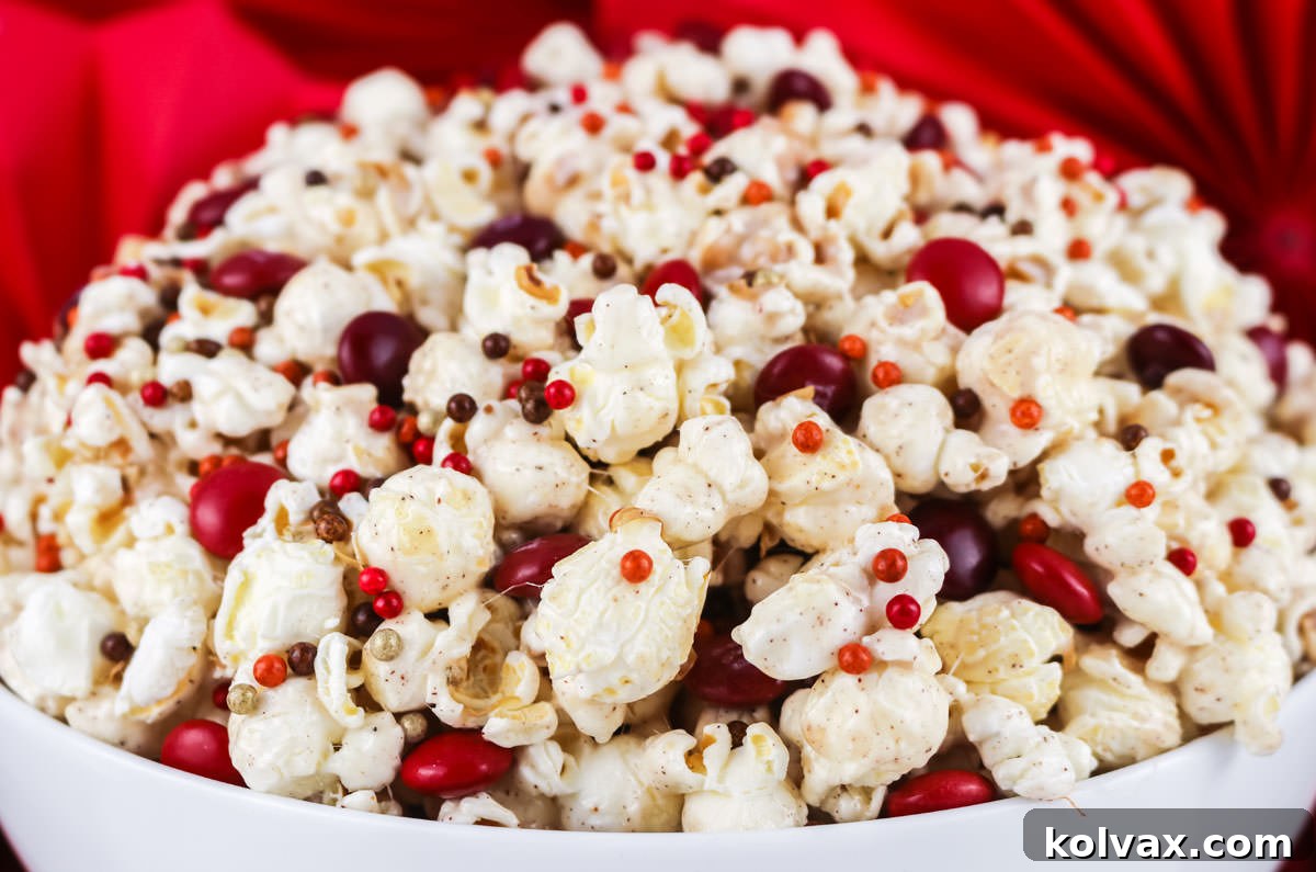 Closeup on a white serving bowl filled with Pumpkin Spice Popcorn sitting in front of a red background, adorned with festive sprinkles.