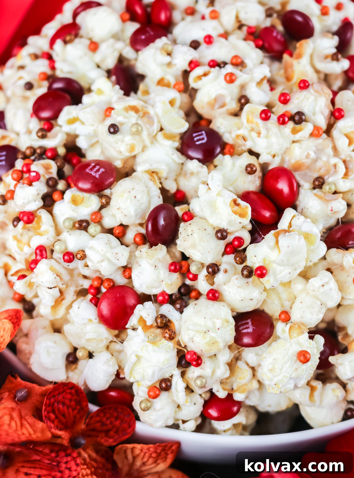 Closeup on a white serving bowl filled with Pumpkin Spice Popcorn, adorned with festive sprinkles and red M&M's.