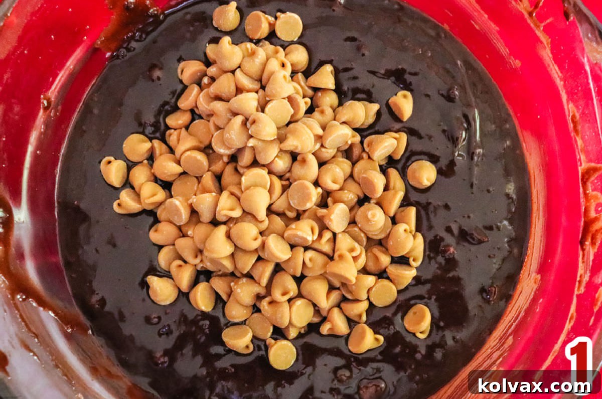 Decadent Peanut Butter Brownie Bars 3 Closeup on a clear mixing bowl filled with rich, dark chocolate brownie batter, generously folded with golden peanut butter chips, ready to be poured into the baking pan.