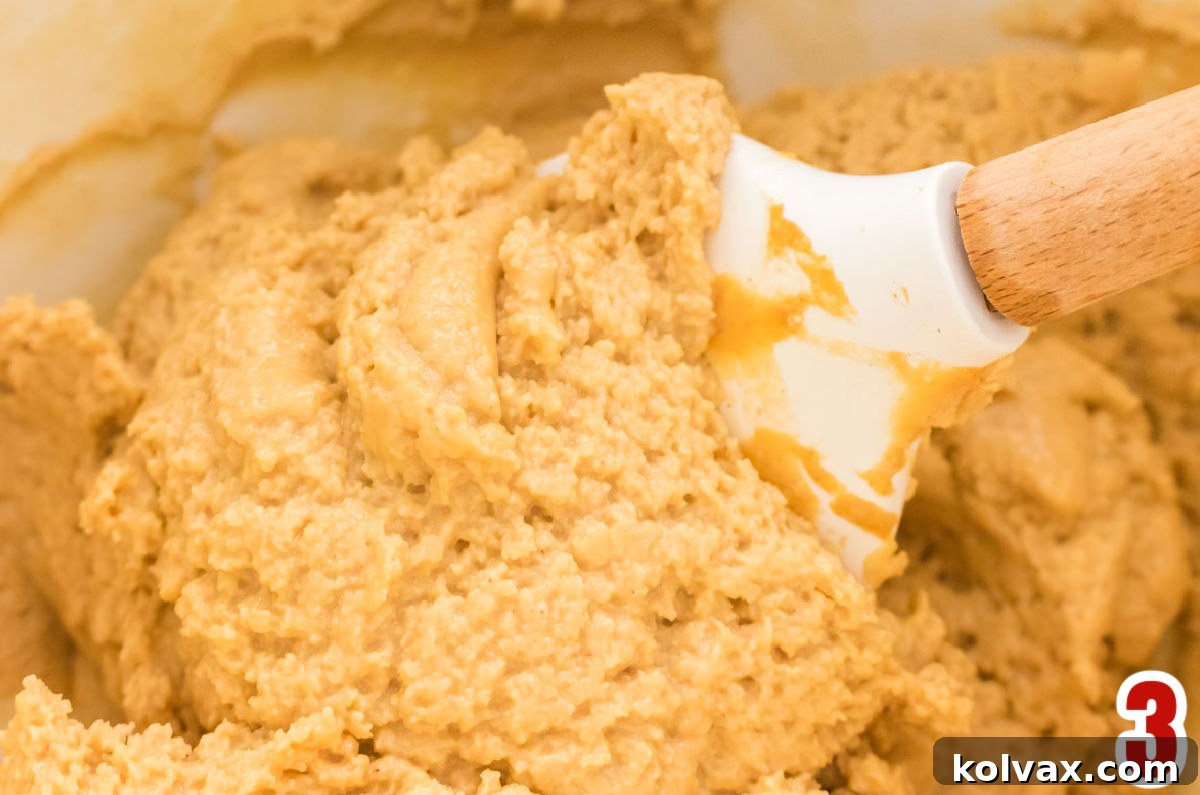 Decadent Peanut Butter Brownie Bars 5 Closeup on a gleaming white mixing bowl overflowing with homemade, fluffy, and creamy Peanut Butter Frosting, with a white spatula resting inside, inviting you to taste its rich texture.