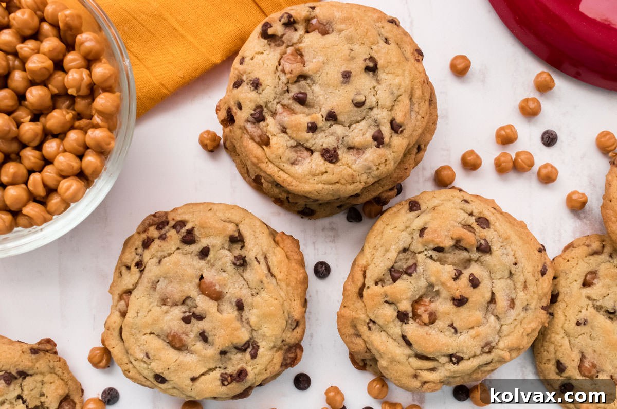 Closeup on three stacks of Caramel Chocolate Chip Cookies sitting on a white table alongside of a glass bowl filled with Caramel Bits.