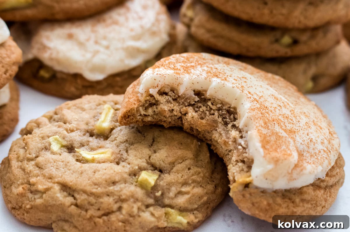 Closeup on two Apple Cookies with Cream Cheese Frosting (one frosted, one not frosted) laying on a white surface, highlighting their soft texture and delicious appeal.