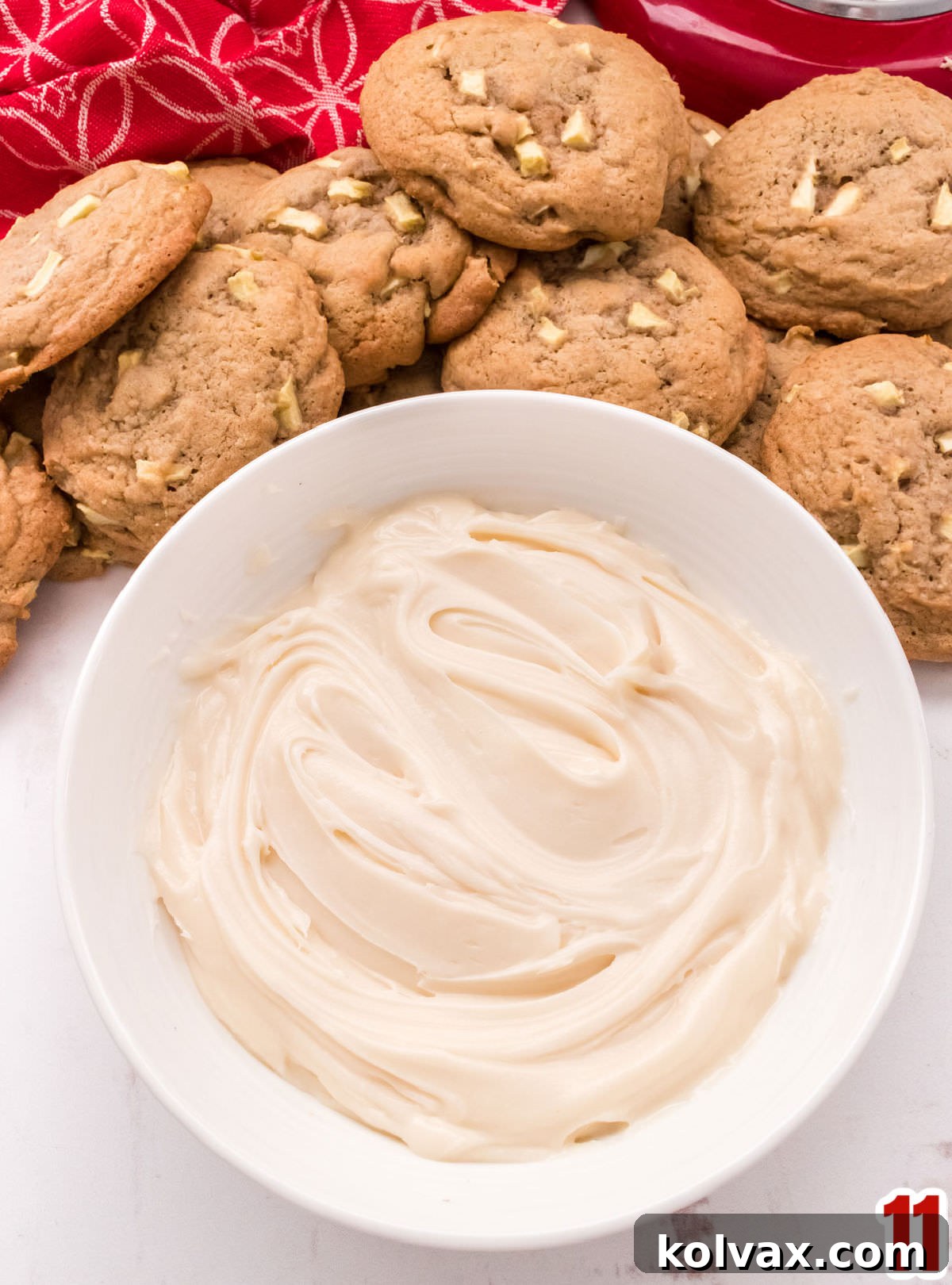 Closeup on a pristine white bowl overflowing with Homemade Cream Cheese Frosting, artfully surrounded by baked Apple Cookies, ready for frosting.