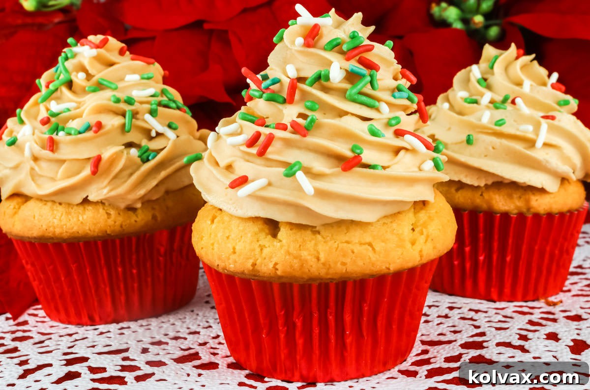 Closeup on three Eggnog Cupcakes with Butter Rum Frosting sitting on a white table cloth, adorned with festive sprinkles.