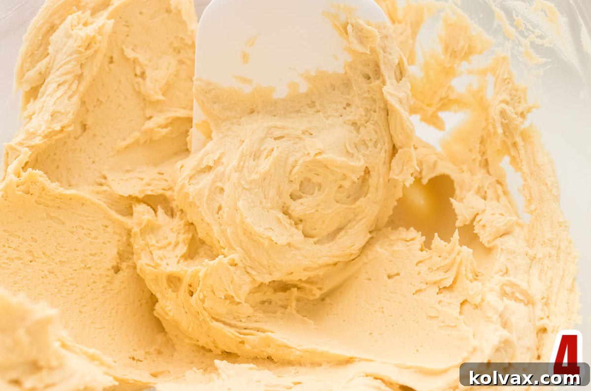 Closeup on a clear glass mixing bowl filled with creamy Butter Rum Frosting and a white wooden spatula resting inside.