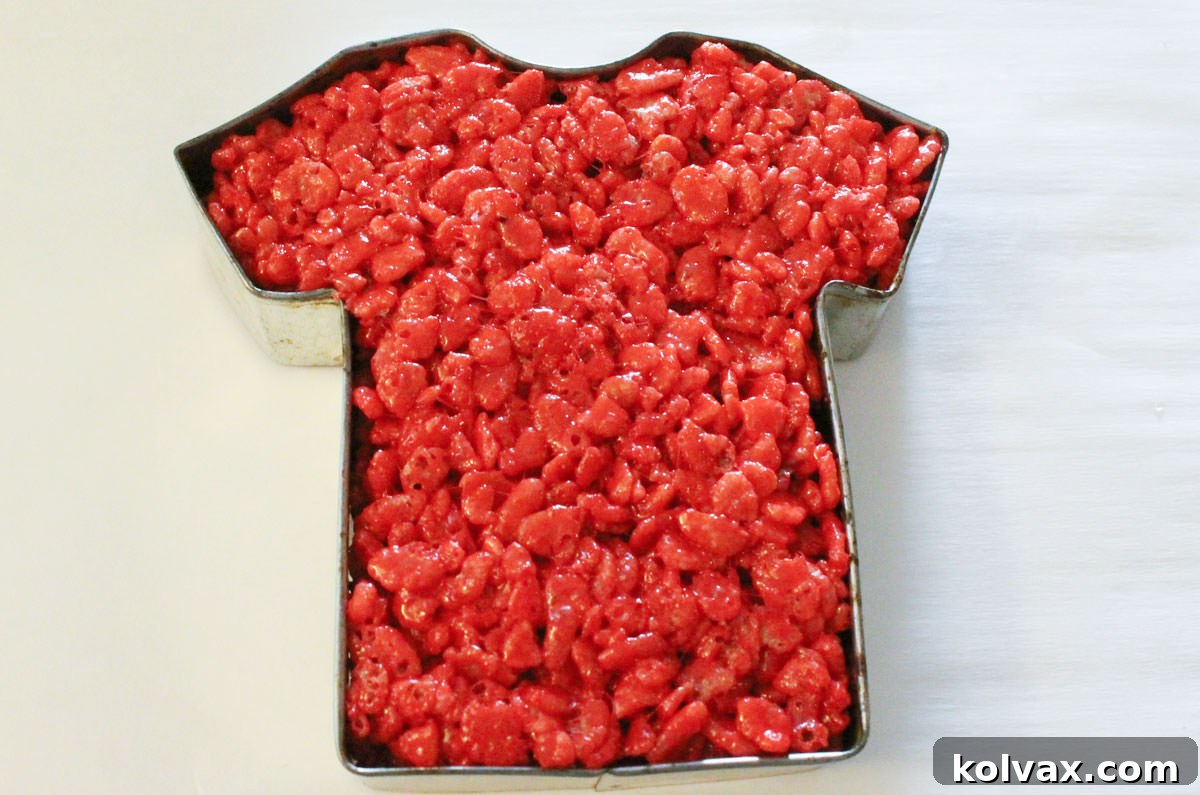 A t-shirt shaped cookie cutter carefully filled with vibrant red Rice Krispie Treat mixture, forming an Atlanta Falcons jersey.