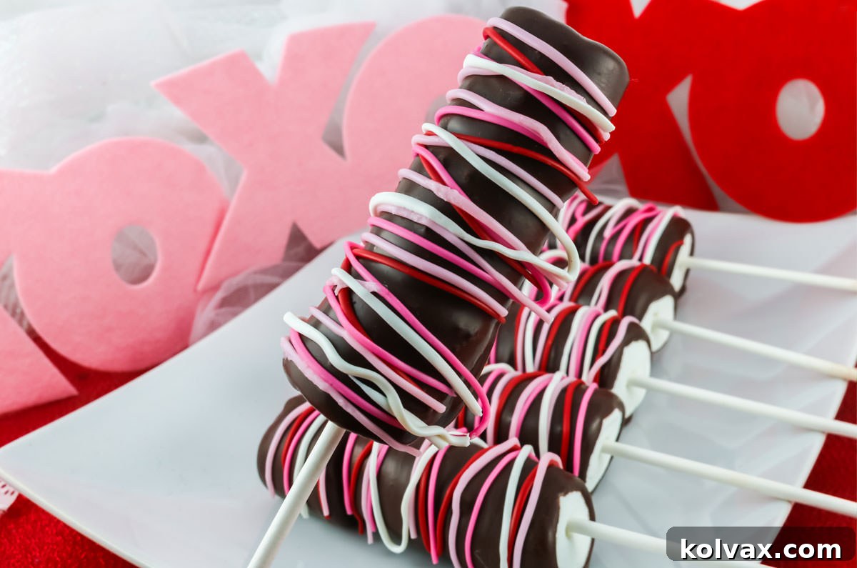 A Valentine's Marshmallow Pop held over a white serving platter holding more chocolate covered marshmallow pops. These pops are a perfect Valentine's Day dessert or treat for loved ones.