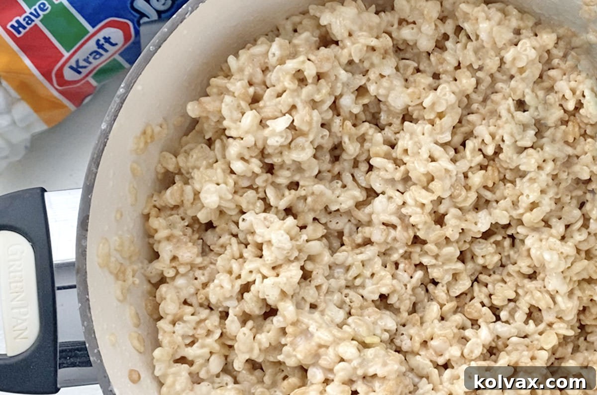 Closeup on a large cooking pan filled with Rice Krispie Treat mixture with a bag of Mini Marshmallows in the background.
