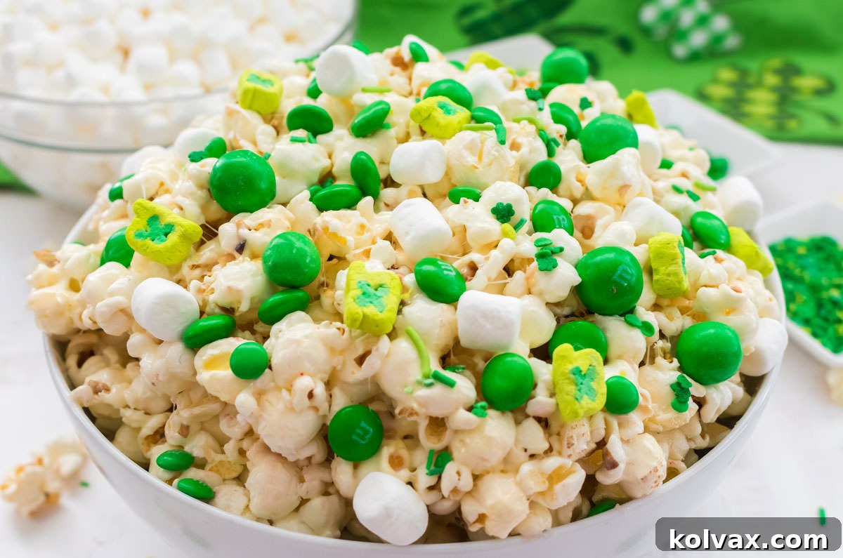 Close up on a bowl of vibrant green St. Patrick's Day Popcorn, adorned with marshmallows, green sprinkles, and green M&M's, set on a white table with a festive St. Patrick's Day linen peeking out.