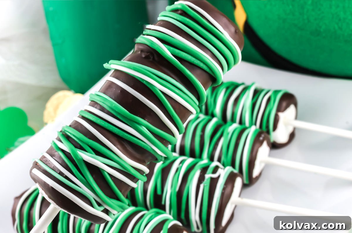 Closeup on a St. Patrick's Day Marshmallow Pop being held over a plate full of other marshmallow pops in front of a leprechaun hat.