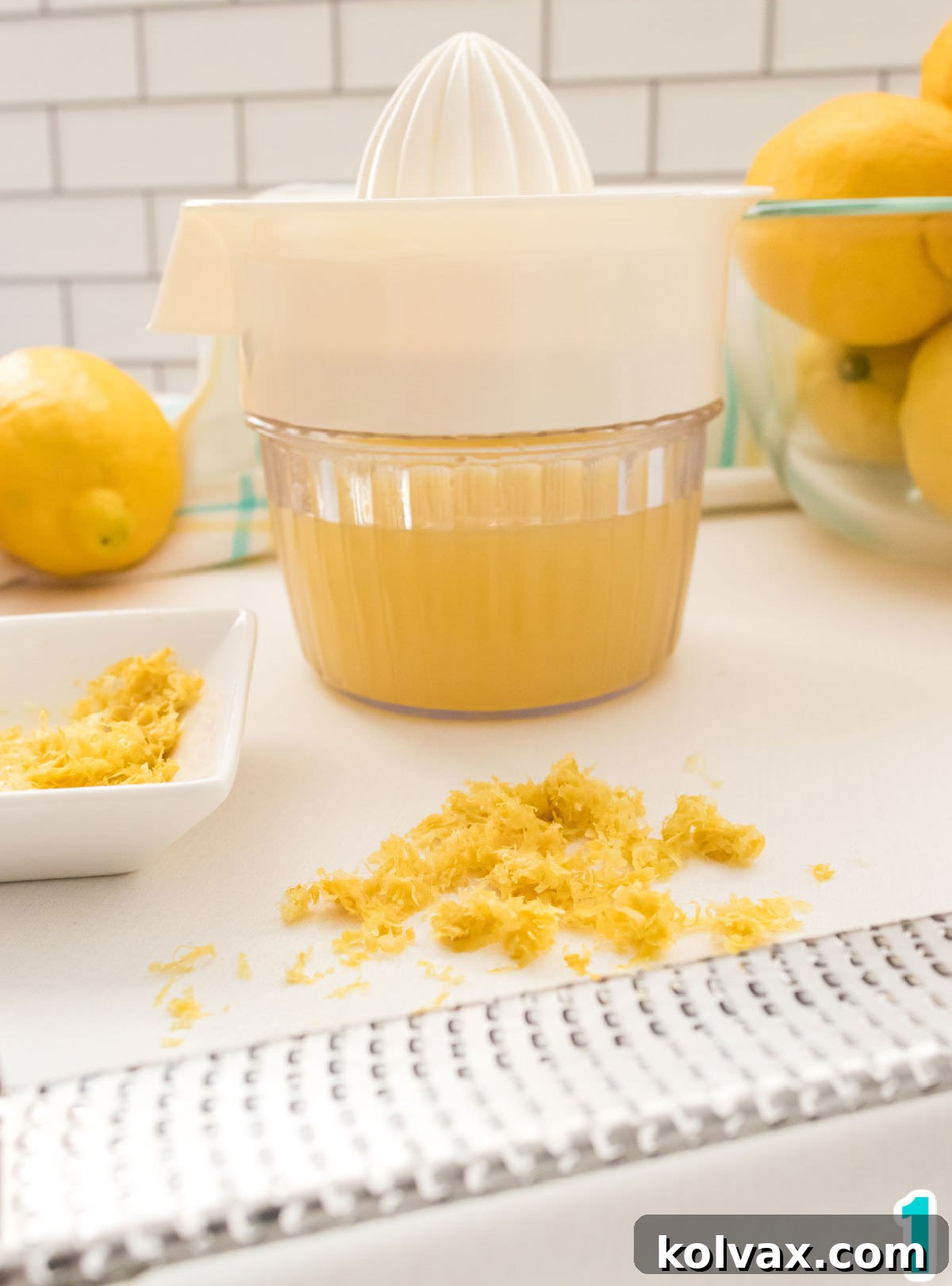A close-up shot of a lemon juicer filled with freshly squeezed lemon juice, positioned in front of a microplane zester containing finely grated lemon zest. This image highlights the fresh lemon preparations essential for baking.