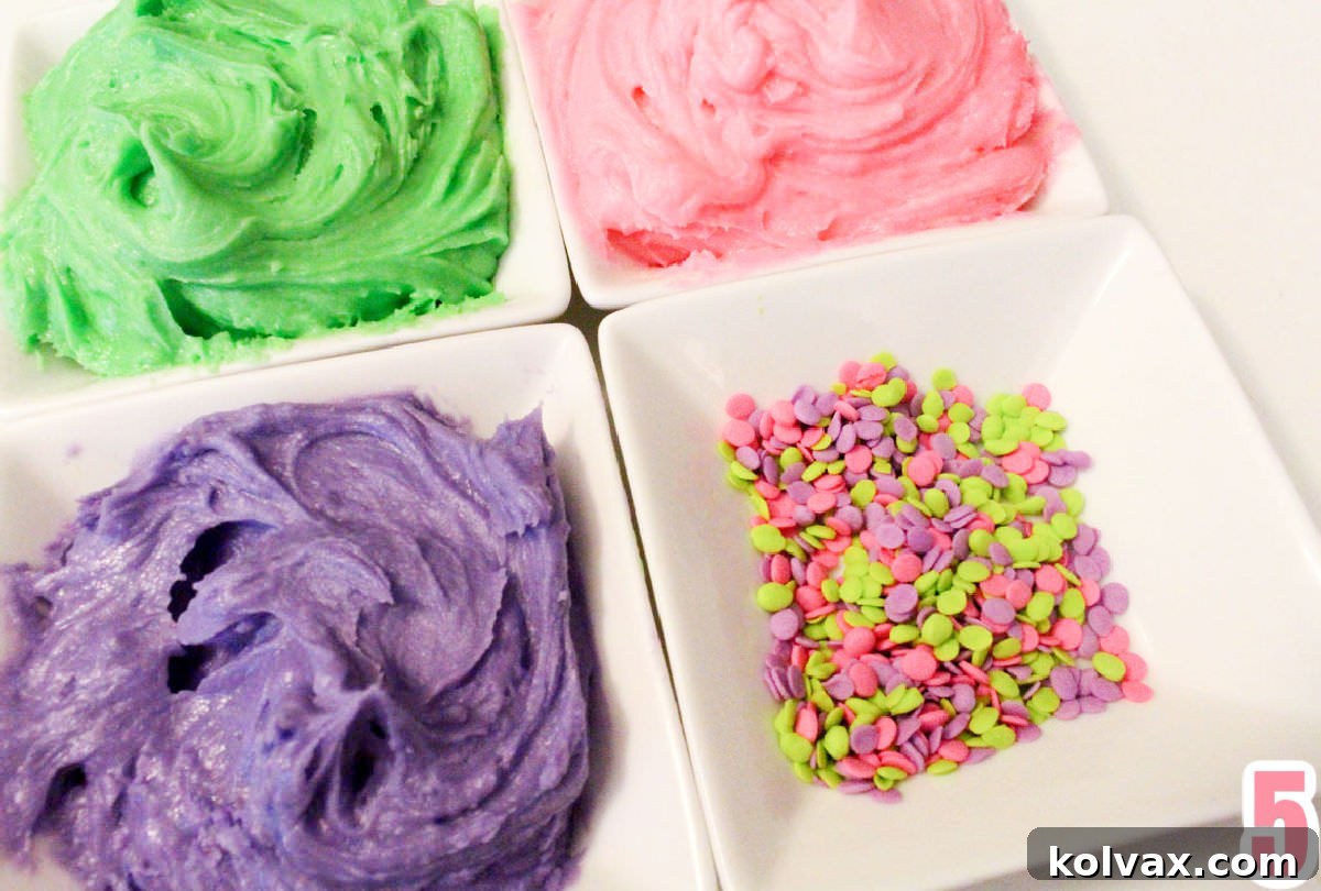 Closeup of four white ramekins filled with vibrant green, pink, and purple buttercream frosting, along with a dish of colorful sprinkles, ready for cookie decorating.