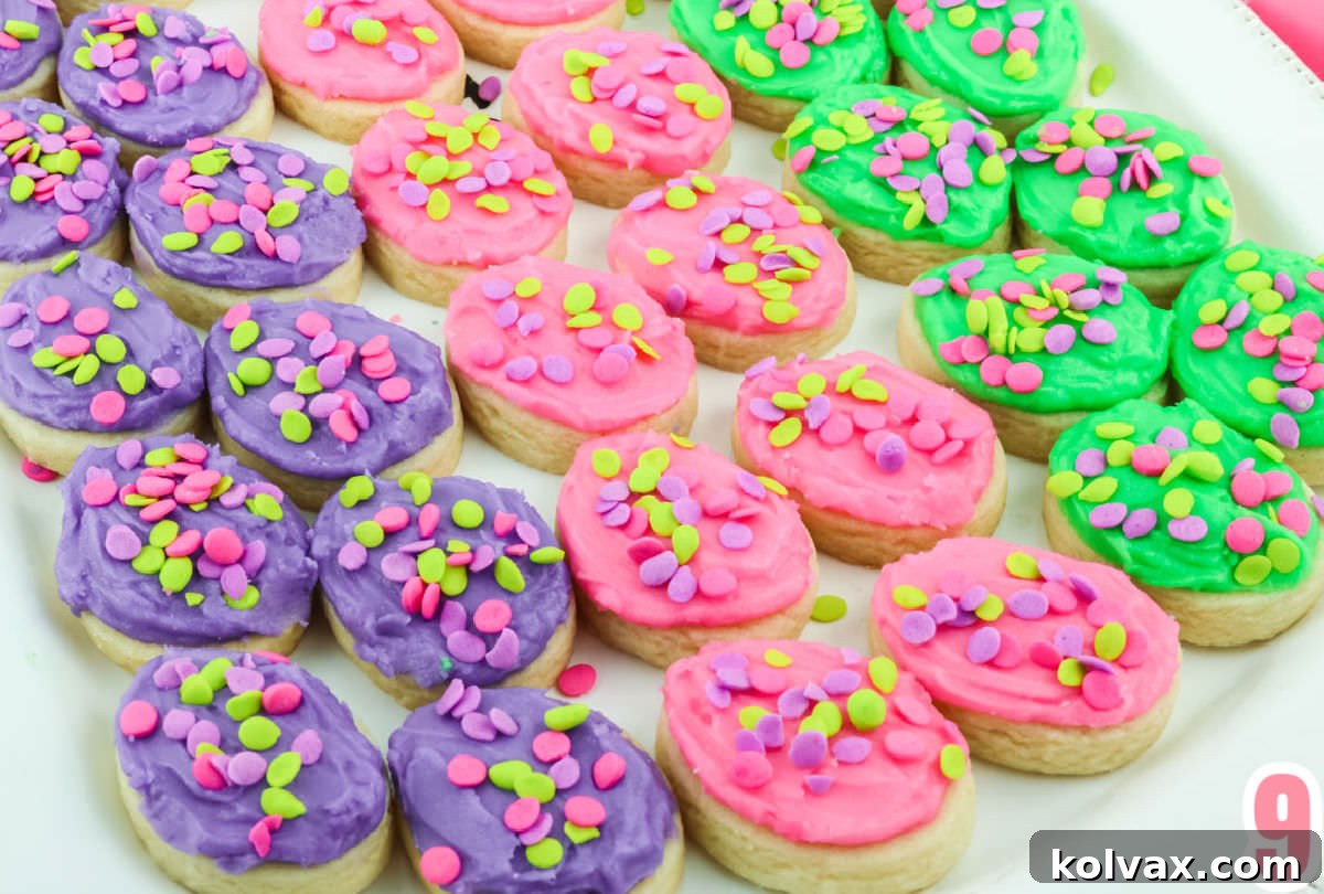 Close up on a white platter covered with three rows of purple, pink and green Easter Egg Sugar Cookies frosted with buttercream frosting and covered in sprinkles, neatly arranged.