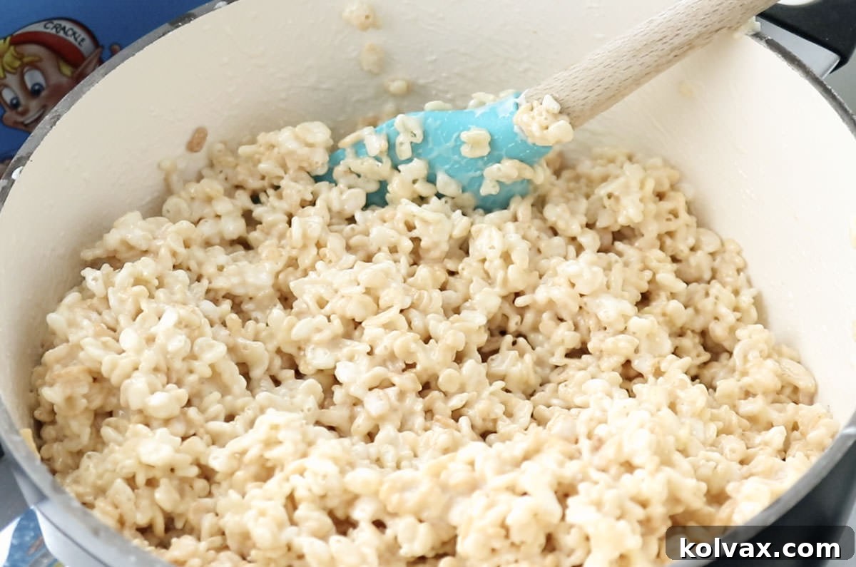White sauce pan filled with Rice Krispie Treat mixture and a blue wooden spatula. This is the perfect base for creating colorful and delicious Easter Rice Krispie Treat Bites.