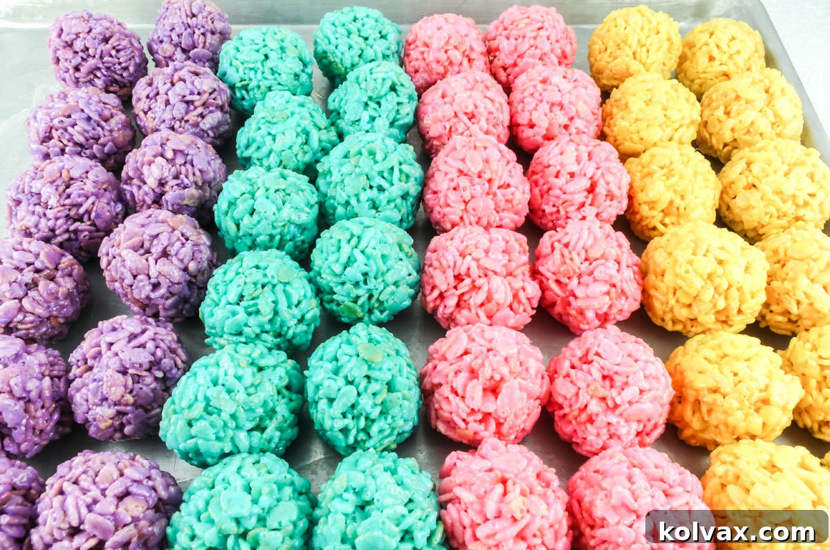 Cookie sheet filled with rows of purple, blue, pink and yellow Rice Krispie Treat Bites, cooling on parchment paper.