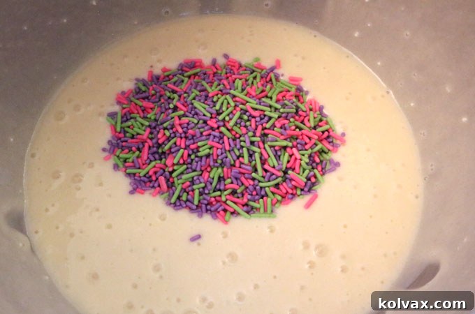 Adding colorful jimmies sprinkles to a bowl of white cake batter.