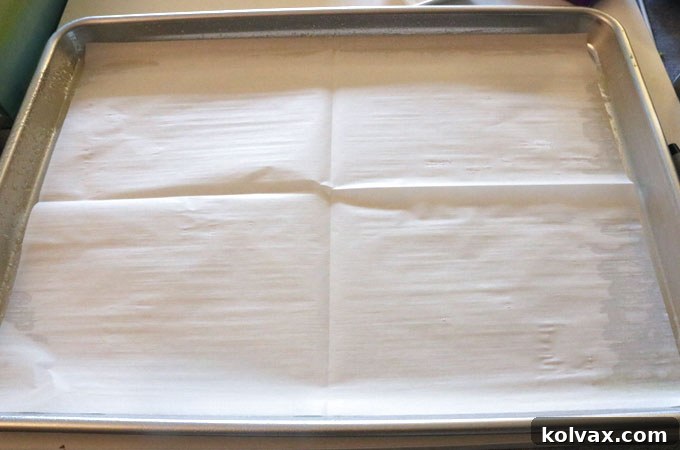 A cookie sheet lined with parchment paper, ready for cake batter.