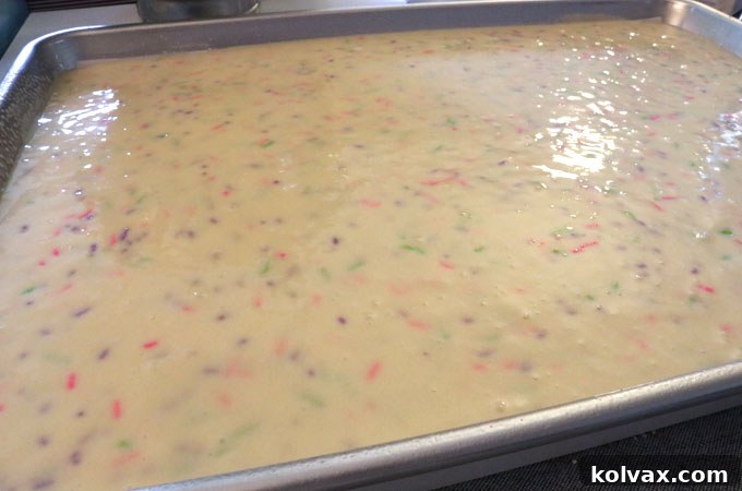 Pouring white cake batter with colorful sprinkles onto a parchment-lined cookie sheet.
