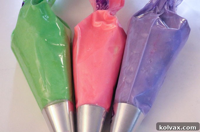 Three pastry bags filled with green, pink, and purple buttercream frosting.
