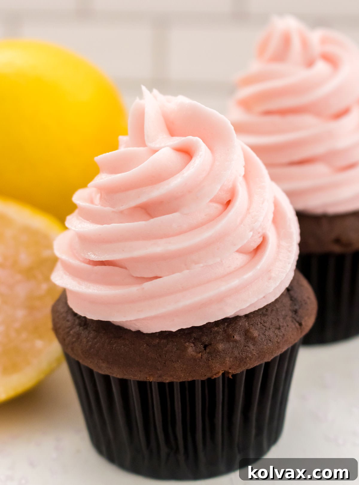 A perfectly frosted chocolate cupcake with The Ultimate Pink Lemonade Frosting, garnished with a fresh lemon slice, embodying a refreshing dessert for spring and summer.