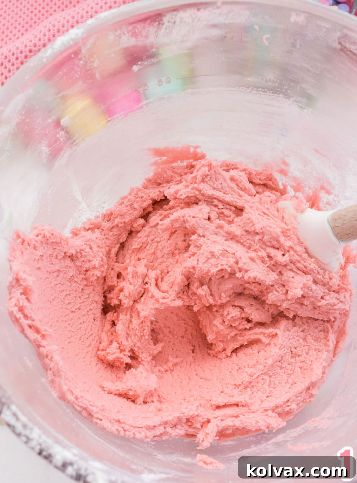 A close-up shot of a clear glass mixing bowl filled with perfectly blended, soft pink sugar cookie dough, ready for the next step.