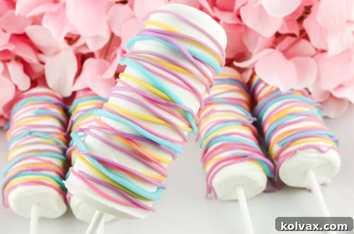 Close up of a Celebration Marshmallow Pop being held up over a white platter covered with more marshmallow pops, showcasing vibrant drizzles.