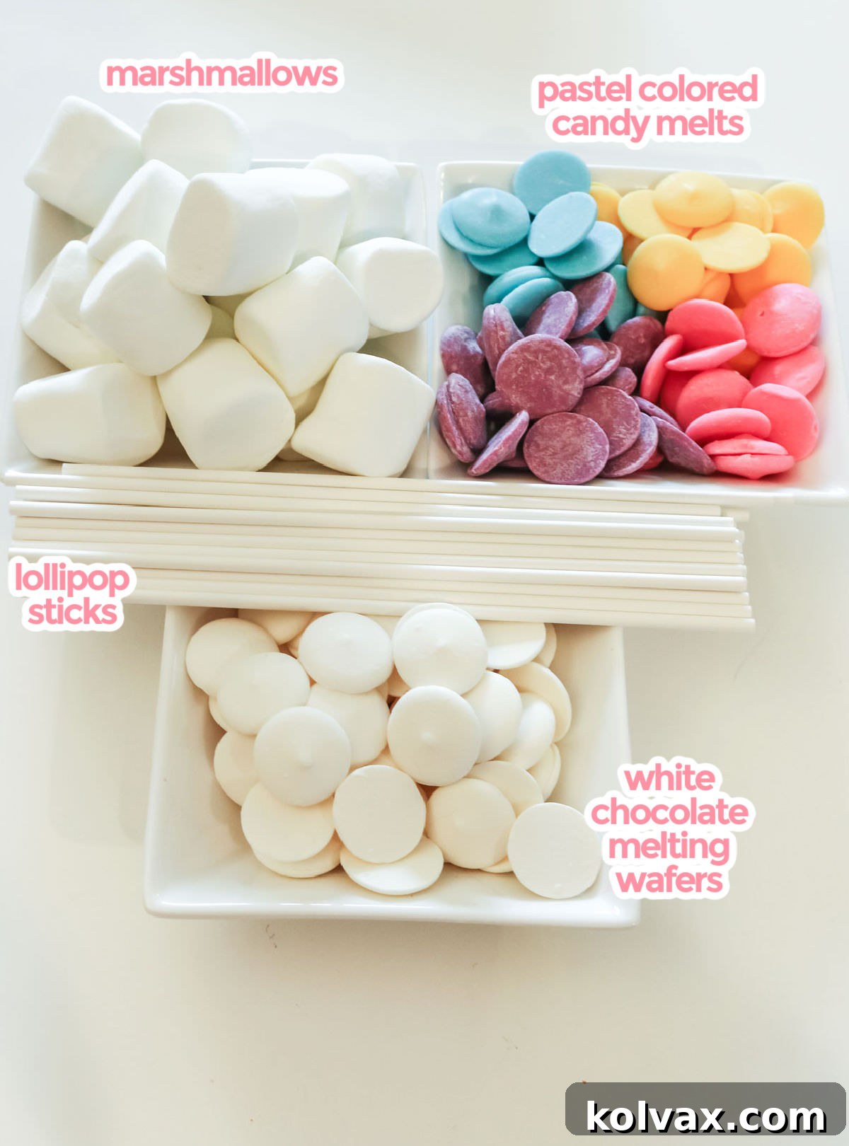All the ingredients necessary to make Celebration Marshmallow Pops including marshmallows, lollipop sticks, white chocolate melting wafers, and pastel colored candy melts arranged on a white surface.