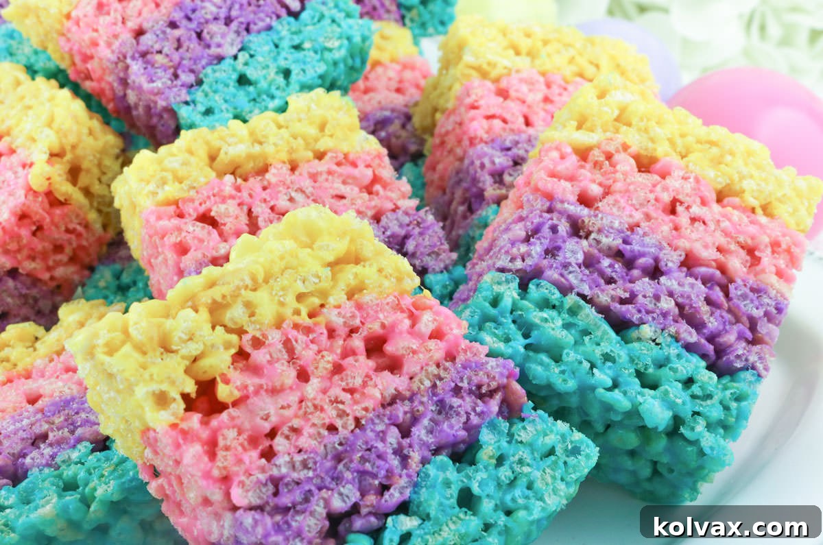Festive Krispie Squares 2 Closeup of brightly colored layered Rice Krispie Treats on a white plate, featuring distinct stripes of blue, purple, pink, and yellow.