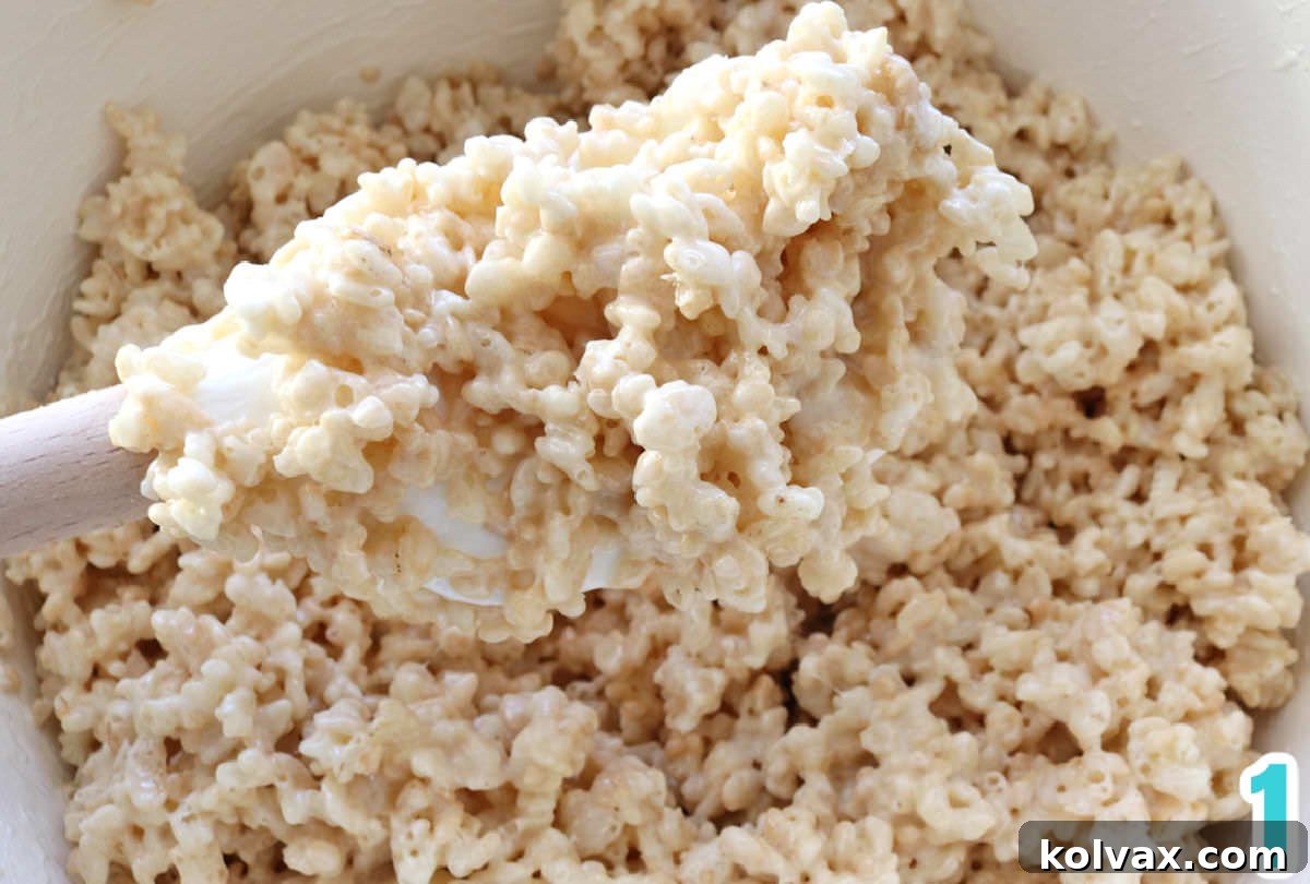 Festive Krispie Squares 3 White saucepan filled with freshly melted marshmallow and butter mixture, stirred with a wooden spatula, ready for food coloring and cereal.