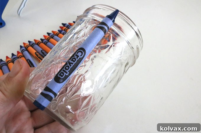 Applying hot glue to the back of a crayon to attach it to a Mason jar