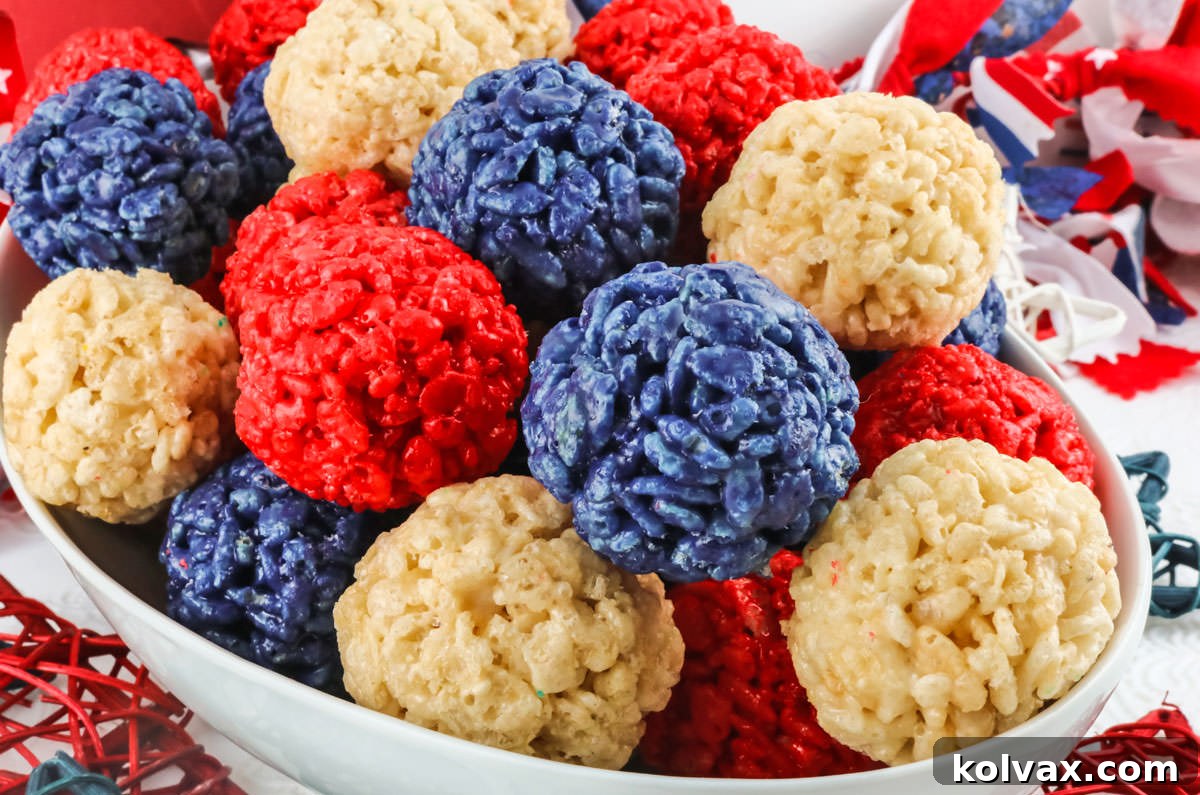 Closeup of a White Bowl filled with Red White and Blue Rice Krispie Treat Bites sitting on a white table decorated with 4th of July decorations.