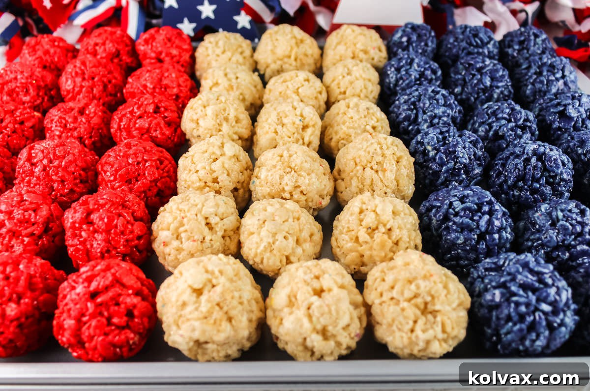 Closeup on a cookie sheet filled with rows of Red White and Blue Rice Krispie Treat Bites with 4th of July decorations in the background.