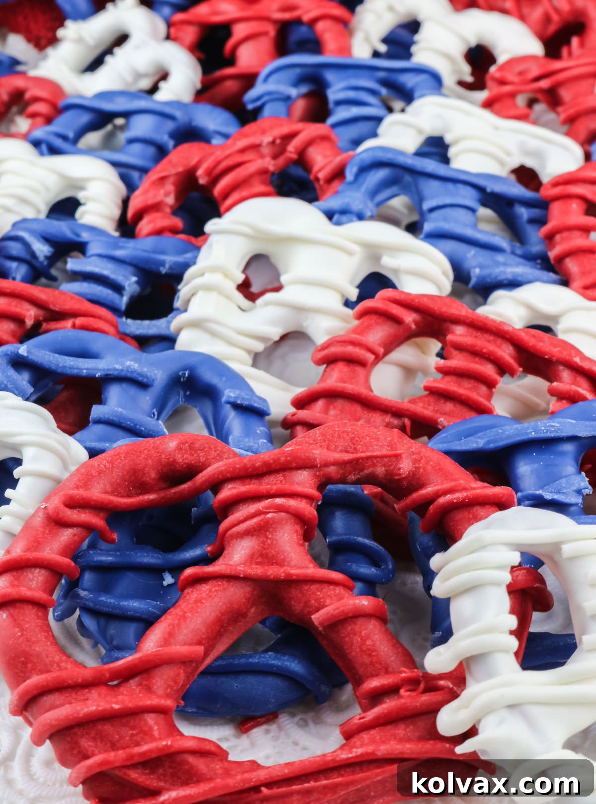 Closeup of many red white and blue Patriotic Pretzels laying on a white surface, showcasing the variety of sizes and colorful candy coatings.