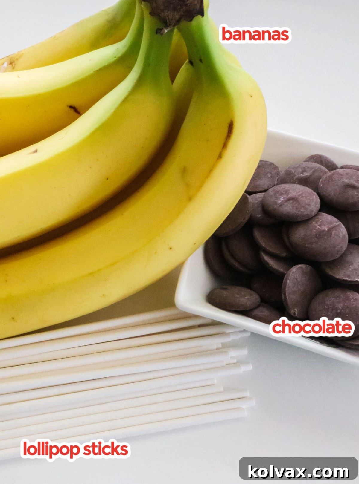 A flat lay of ingredients needed to make Frozen Chocolate-Covered Bananas, including ripe bananas, chocolate melting wafers, and lollipop sticks on a kitchen counter.