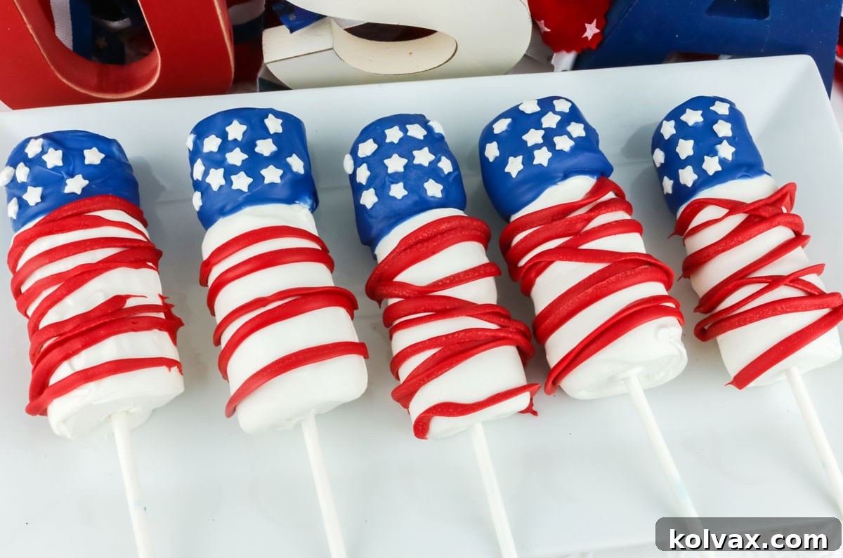 Red White and Blue Marshmallow Pops 2 Five American Flag Marshmallow Pops laying on a white serving platter in front of a red white and blue USA sign. A perfect 4th of July dessert.